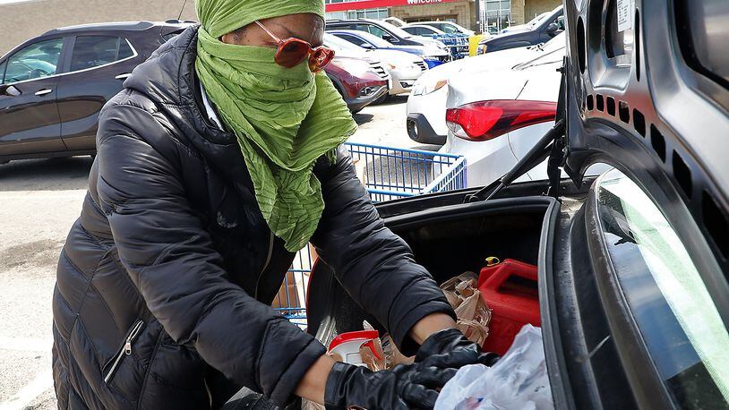 Ernnee Webber wears a scarf over her head and face and gloves as she puts her groceries in the trunk of her car Friday at Meijer in Springfield. Webber said she tried to find some medical masks but every place was sold out so she made her own. BILL LACKEY/STAFF