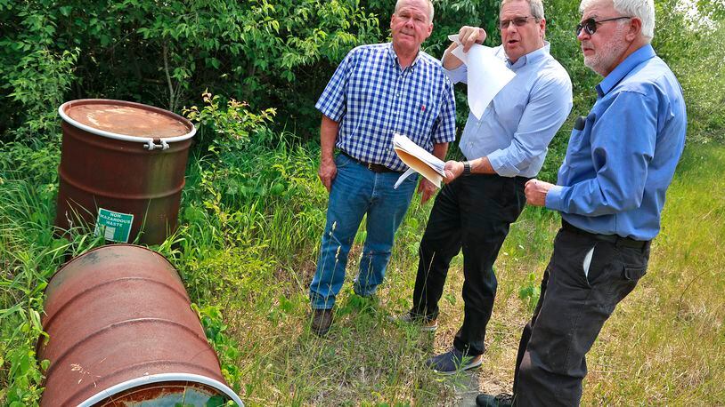 Bob Rule, from the Potentially Responsible Party group, center, along with German Twp. Trustee Rodney Kaffenbarger, left, and Larry Ricketts from People For Safe Water go over the layout for the Tremont City Barrel Fill on Wednesday, June 7, 2023. The barrels, at left, were empty but used during testing. BILL LACKEY/STAFF