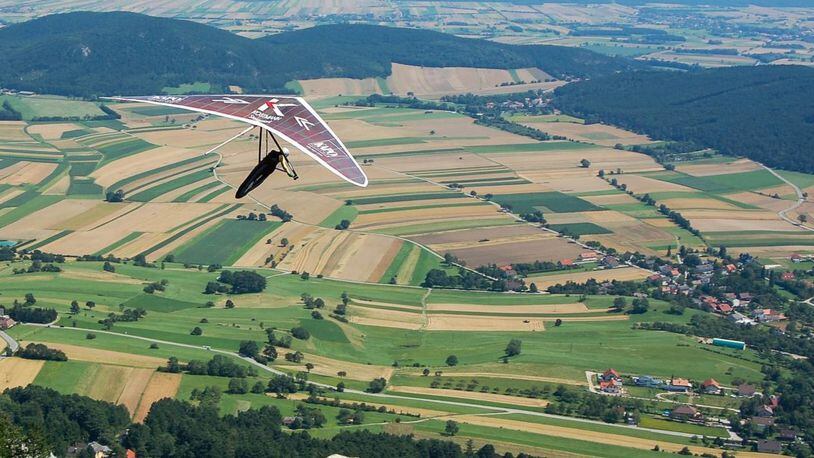A hang glider soars above the countryside enjoying a beautiful vista of the earth below.