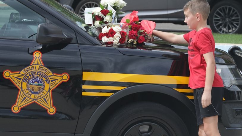 A boy puts flowers on the hood of a Clark County Sheriff's vehicle set up on the Springfield City Hall Plaza as a memorial for Deputy Matthew Yates Monday. BILL LACKEY/STAFF