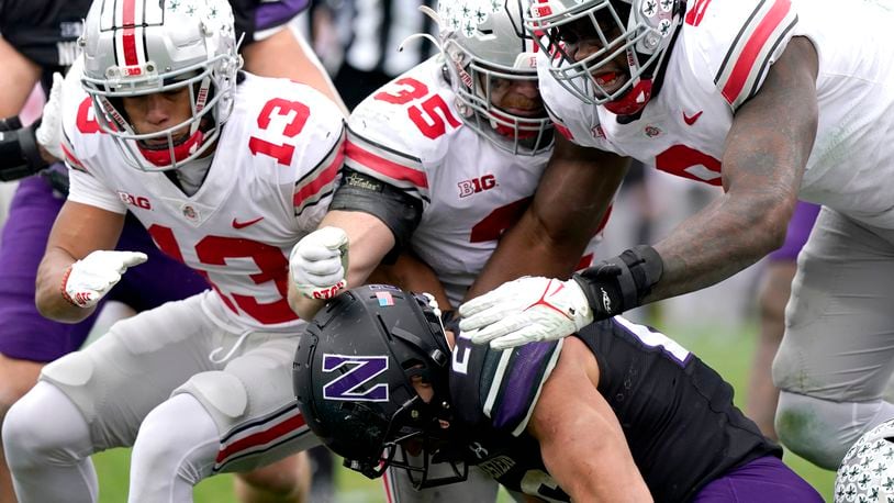 Northwestern running back Evan Hull, bottom, is tackled by Ohio State safety Cameron Martinez, left, linebacker Tommy Eichenberg and defensive end Zach Harrison, right, during the second half of an NCAA college football game, Saturday, Nov. 5, 2022, in Evanston, Ill.  (AP Photo/Nam Y. Huh)
