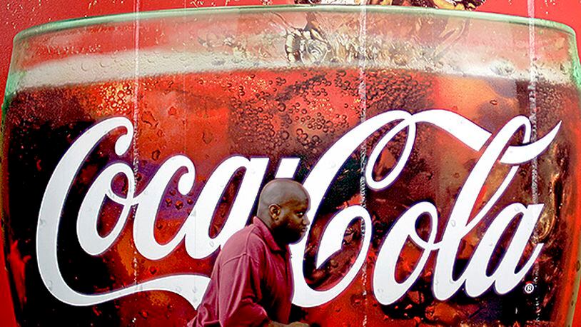 FILE- In this Monday, July 16, 2012, photo, a man walks past a billboard for Coca-Cola outside a convenience store in Atlanta. Coca-Cola on Thursday, Jan. 8, 2015 said it's cutting between 1,600 and 1,800 jobs globally as part of an ongoing push to trim costs. (AP Photo/David Goldman, File)