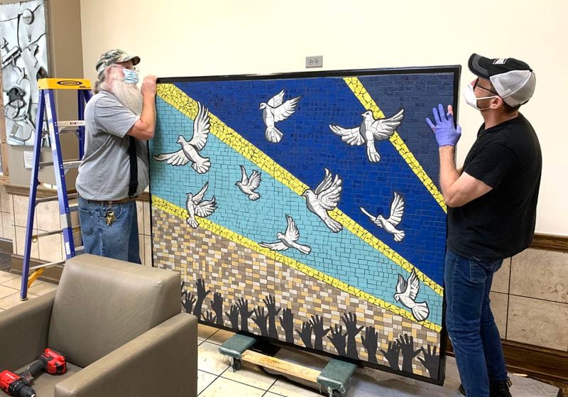 Tim Fitzgerald (left) a carpenter with the City of Dayton and Michael Goodson, curator and director of programming at The Co., hang "9 Doves" in the lobby of Dayton City Hall earlier this year. The mural, designed by Jes McMillan, founder of the Mosaic Institute of Greater Dayton, was created with help from the community in response to the mass shooting in the Oregon District. LISA POWELL / STAFF