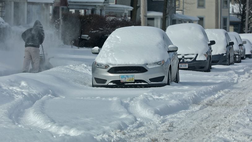 A man cleans off the sidewalk along a row of cars, buried in the snow, on East Madison Street in Springfield. BILL LACKEY/STAFF