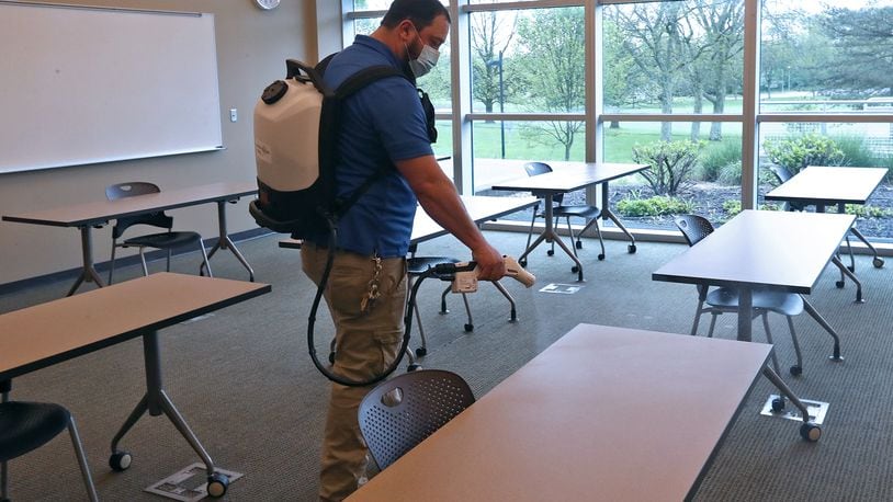 Ryan Green, Maintenance Supervisor at Clark State, sanitizes a classroom with a Protexus Electrostatic Sprayer like his crew will do every evening when classes are finished. Studens are also positioned six feet apart in the classrooms and hand sanitizers are outside every classroom. BILL LACKEY/STAFF
