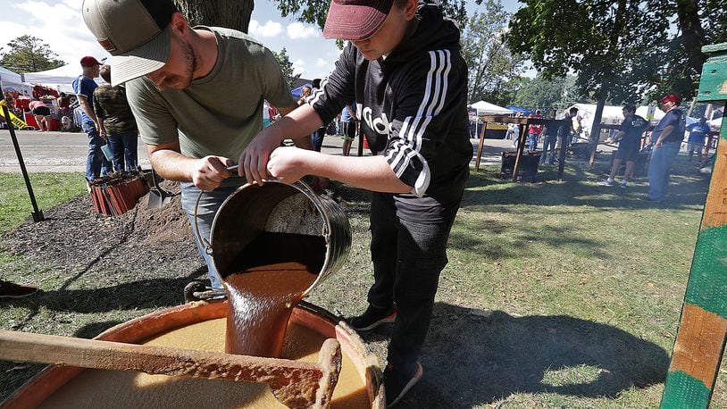 Jacob Juergens, left, and Caelek Stephany, both members of the Murphy family, pour the brown sugar mixture into one of the cauldrons of cooking apple butter Saturday at the Enon Apple Butter Festival. BILL LACKEY/STAFF 