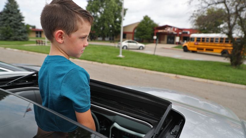 Ty Siri keeps an eye out for his big sister as he stands through the sunroof of his mother's car while waiting for school to release early at Indian Valley School in Enon on Aug. 26. The Greenon school district was one of several schools that released early because of the heat. BILL LACKEY/STAFF