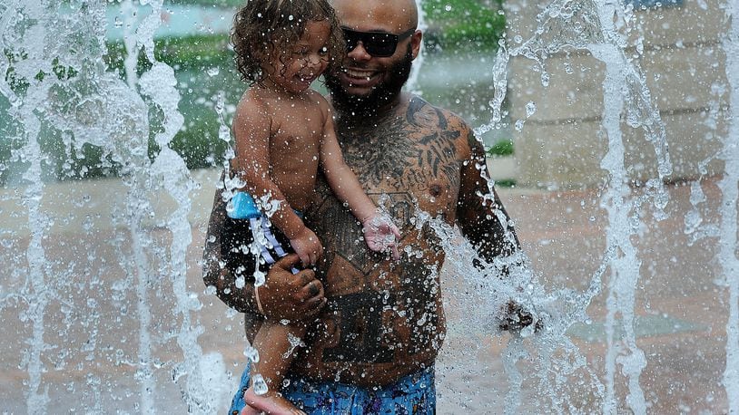 Chris Harris cools off Tuesday July 25, 2023 with his son Cali, age 2, at the splash pad at the Riverscape. MARSHALL GORBY\STAFF