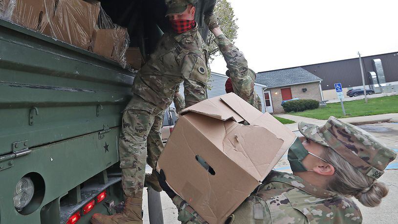 Ohio Army National Guard Spc Logan Wilson hands off a box of food to Sgt Makayla Scharber as they deliver food from the Second Harvest Food Bank to hungry residents in New Carlisle Friday. BILL LACKEY/STAFF