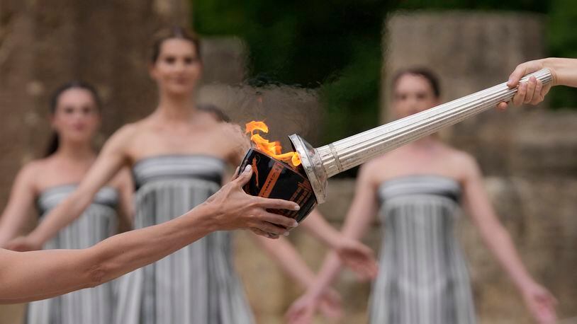 FILE - Actress Mary Mina, playing high priestess, right, lights a torch during the official ceremony of the flame lighting for the Paris Olympics, at the Ancient Olympia site, Greece, April 16, 2024. The Olympic torch finally enters France when it reaches the southern seaport of Marseille on Wednesday May 8, 2024, on an armada from Greece. After leaving Marseille a vast relay route will be undertaken before the torch's odyssey ends on July 27 in Paris. (AP Photo/Thanassis Stavrakis, File)