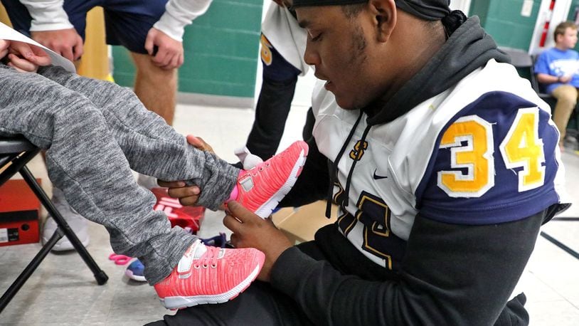 Springfield Wildcats running back, Tay’Veon Smoot, helps a young girl try on a pair of bright pink shoes Tuesday as members of the football team, Jr. ROTC, Cedarville University School of Nursing and others volunteer their time fitting shoes on the feet of needy children at Simon Kenton Elementary Tuesday. The shoes were part of teh Shoes 4 the Shoeless program, which has delivered more than 50,000 pairs of shoes and socks to children in the Dayton and Springfield area. The Shoes 4 the Shoeless program will be visiting 10 schools in the Springfield district. BILL LACKEY/STAFF