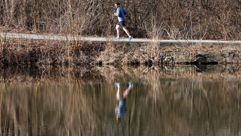 A man is reflected in the water at Hosterman Lake as he takes advantage of the sunshine in this March 1, 2023, photo as he runs through George Rogers Clark Park. BILL LACKEY/STAFF