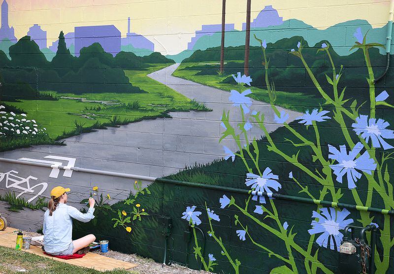 Artist Kelley Booze works on the 2021 Jericho Project mural that welcomes cyclists to Springfield as they travel north along the bike path near the intersection of Leffel Lane and South Yellow Springs Street.  BILL LACKEY/STAFF
