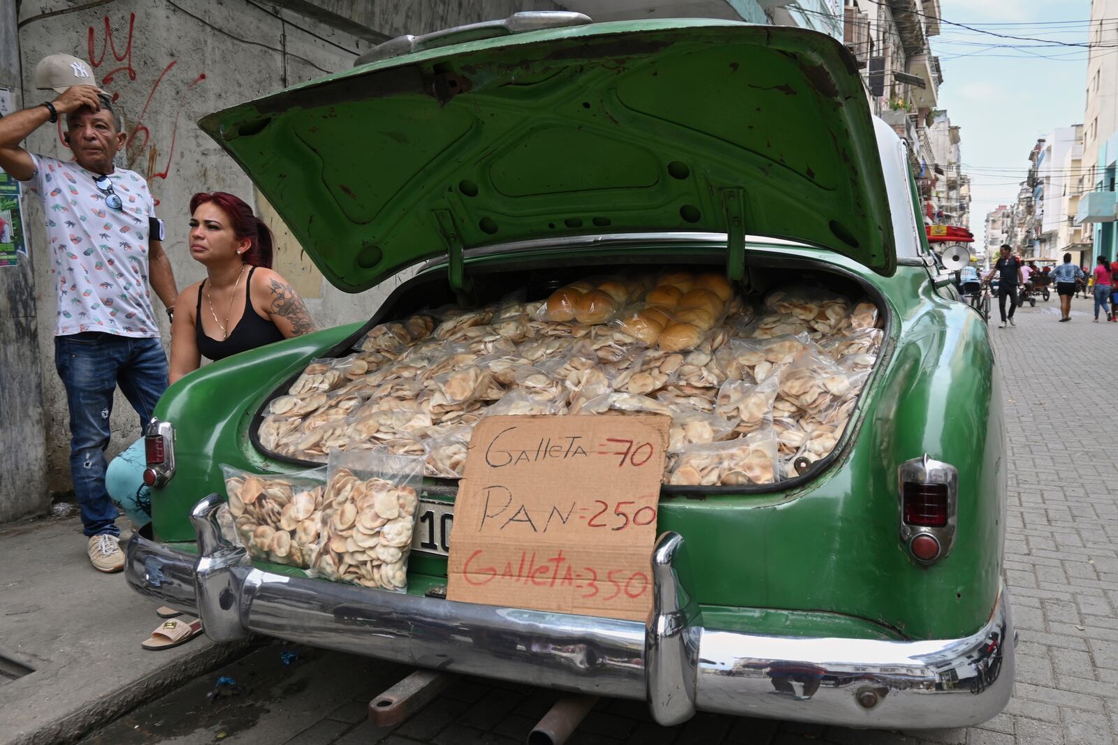 Vendors wait for customers next to the trunk of their American classic car stuffed with homemade crisps and bread, in Havana, Cuba, Tuesday, July 15, 2025. (AP Photo/Jorge Luis Baños)