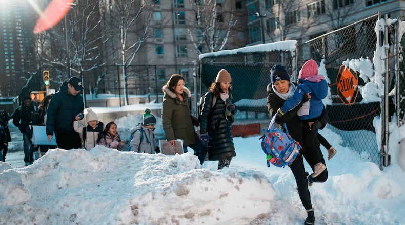 A woman carries a child over piles of plowed snow as she walks a girl to school, Tuesday, Feb. 24, 2026, in New York. (AP Photo/Eduardo Munoz Alvarez)
