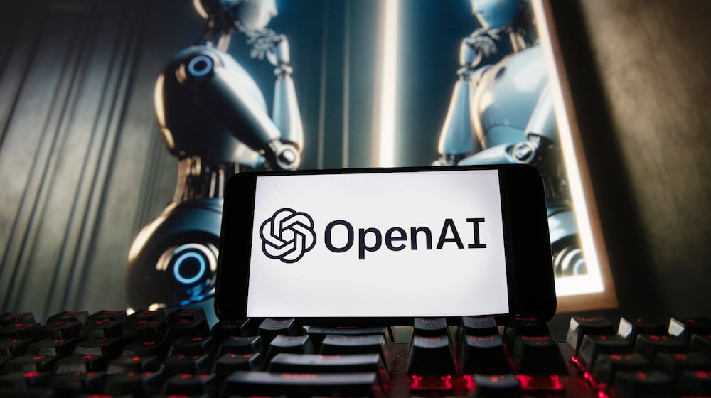 FILE - The OpenAI logo is displayed on a cellphone with an image on a computer monitor generated by ChatGPT's Dall-E text-to-image model, Dec. 8, 2023, in Boston. (AP Photo/Michael Dwyer, File)