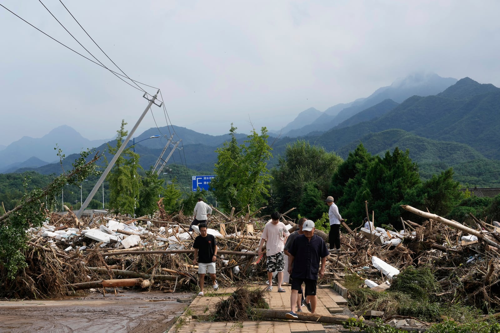 Local residents walks in front of a damaged road littered with broken tree branches after a heavy rains in Taishitun Town, Miyun district on the outskirts of Beijing, China, Monday, July 28, 2025. (AP Photo/Mahesh Kumar A.)