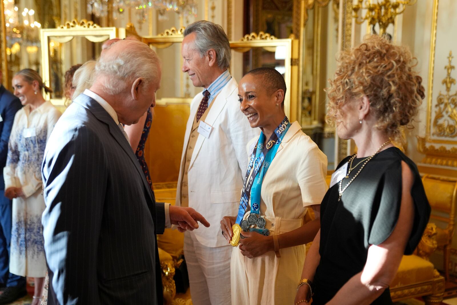 Britain's King Charles III speaks with broadcaster and presenter Adele Roberts, wearing her medals from the TCS London Marathon and Abbott World Marathon Majors, during a reception in Buckingham Palace, London, in celebration of community-based initiatives raising awareness about cancer and supporting those living with cancer, Wednesday April 30, 2025. (Andrew Matthews/Pool Photo via AP)
