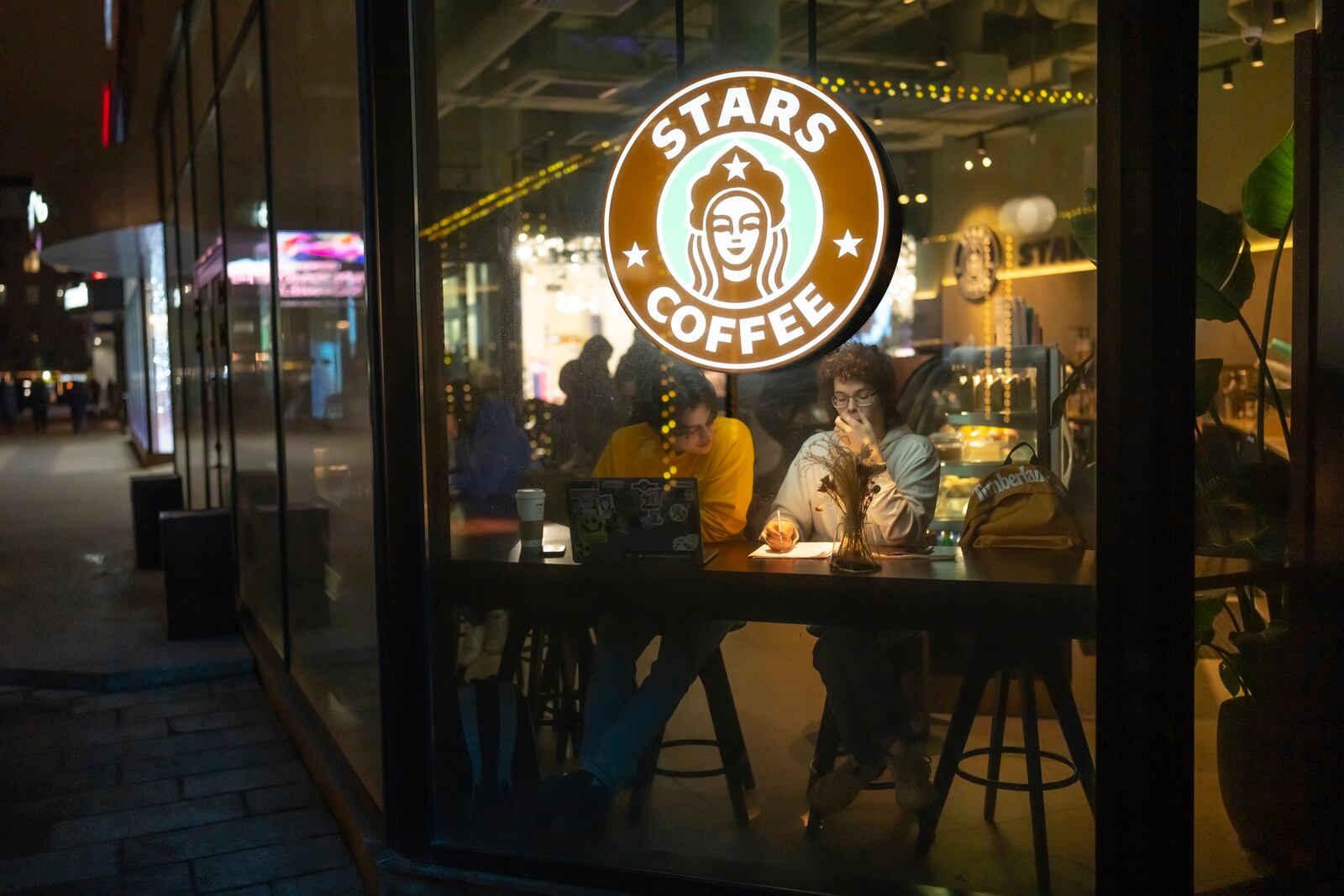 FILE - Patrons sit near the illuminated logo of a newly opened Stars Coffee cafe in the former location of a Starbucks in Moscow, Russia, on Jan. 24, 2023. (AP Photo/Alexander Zemlianichenko, File)