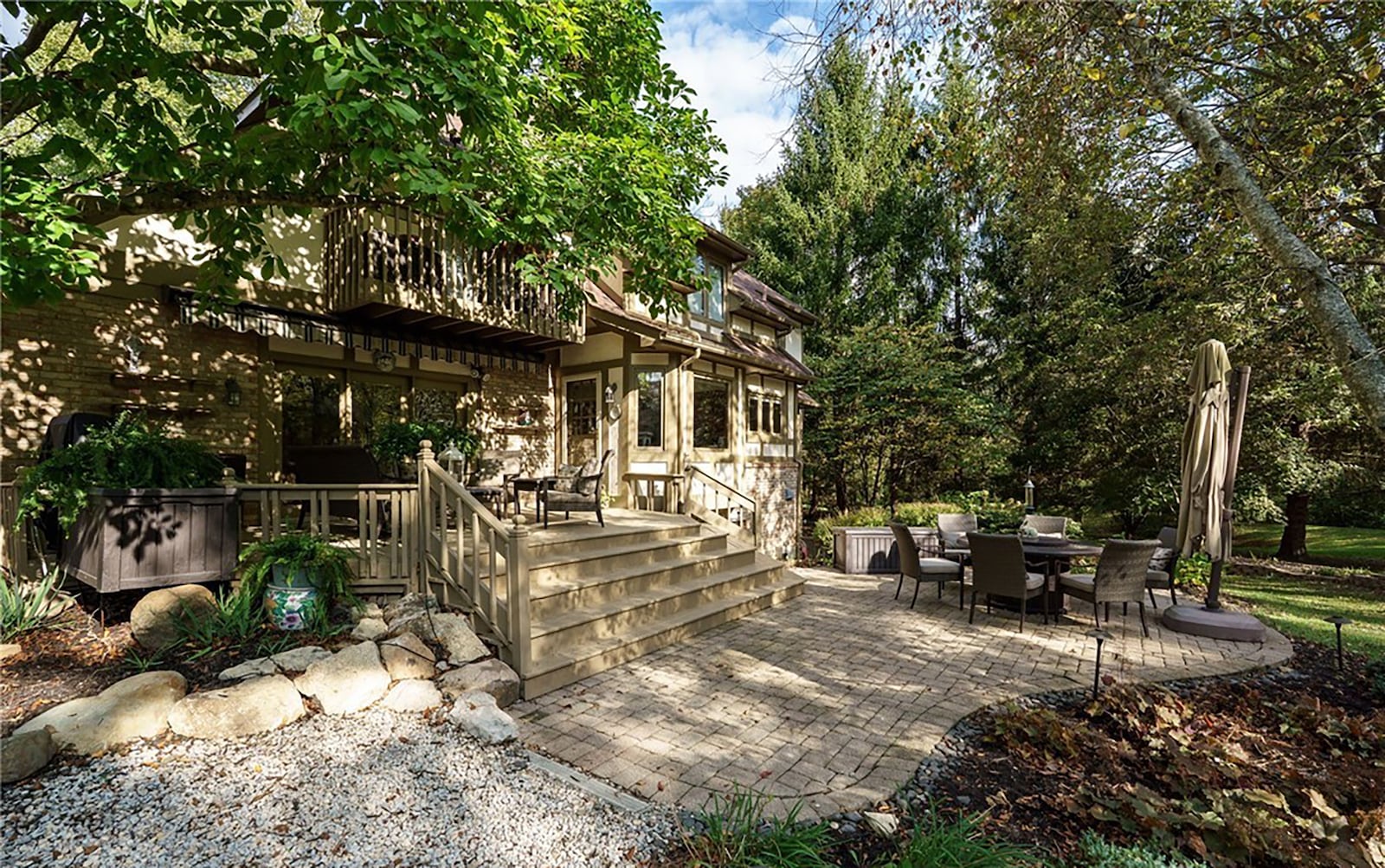 The heavily wooded back yard has a paver patio and raised wood deck with railings and an awning. CONTRIBUTED