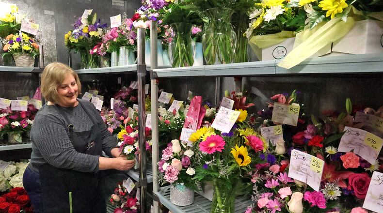 Amy Galbreath sets a flower arrangement in the cooler with dozens of others Thursday at Schneider's Florist. Schneider's is not facing a flower shortage, but many other local florists are. BILL LACKEY/STAFF