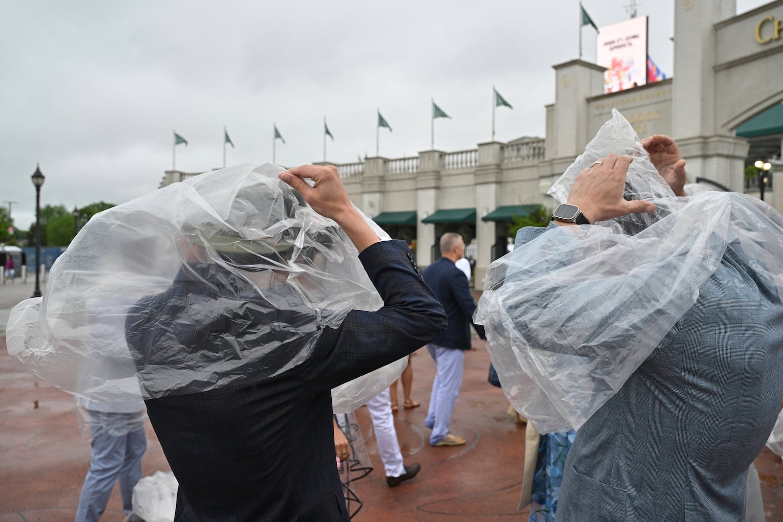 People use plastic in an attempt to stay dry during a drizzle at Churchill Downs before the 151st running of the Kentucky Derby horse race Saturday, May 3, 2025, in Louisville, Ky. (AP Photo/Jon Cherry)