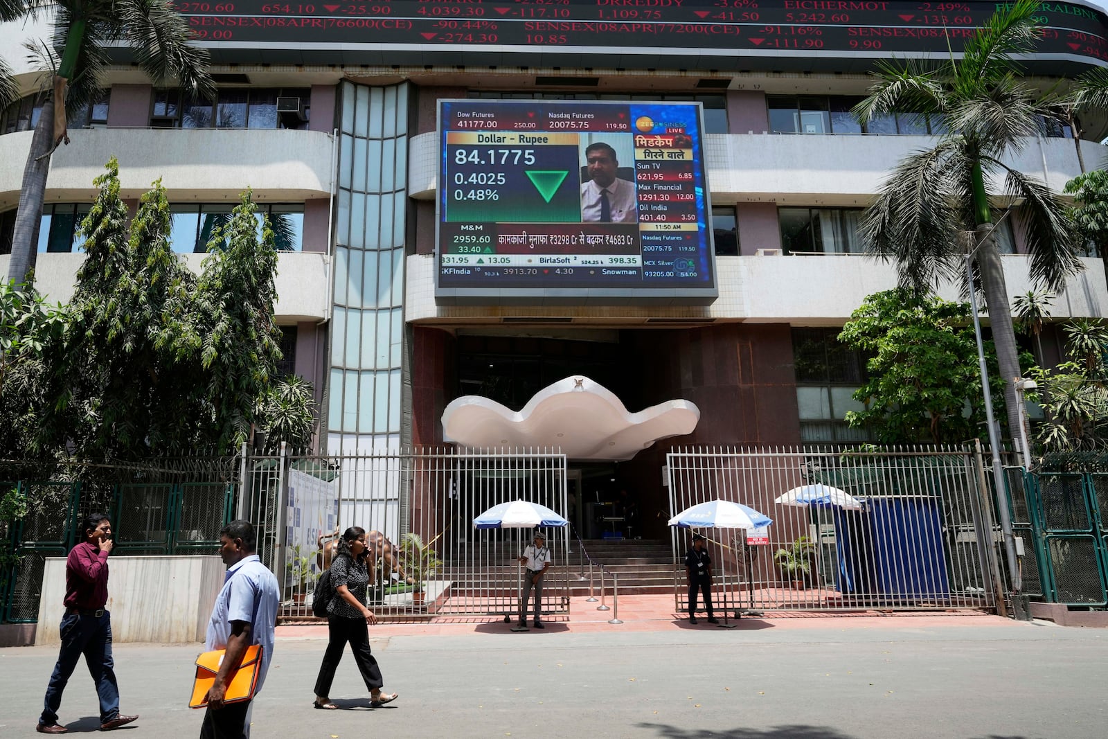 People walk past a live screen on the facade of Bombay Stock Exchange (BSE) building in Mumbai, India, Monday, May 5, 2025. (AP Photo/Rajanish Kakade)