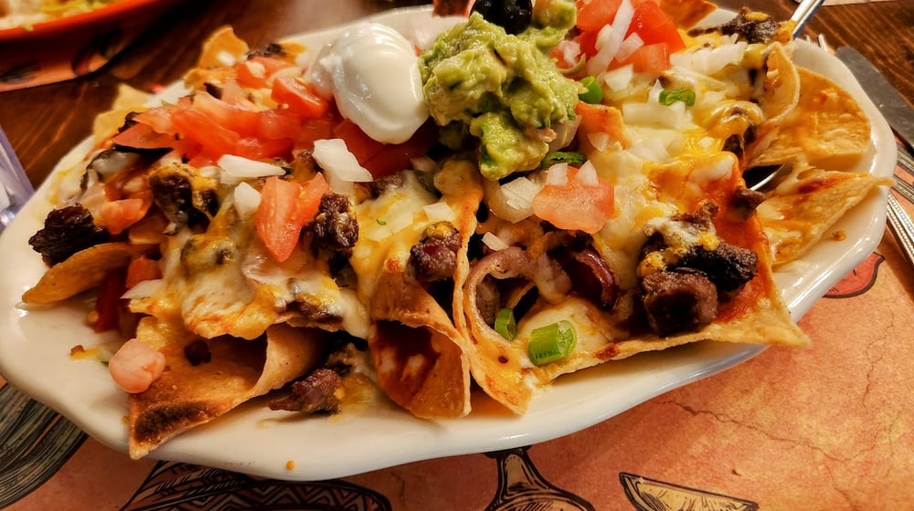 A heaping plate of corn tortilla chips piled high with melted cheese and assorted toppings. ISTOCK