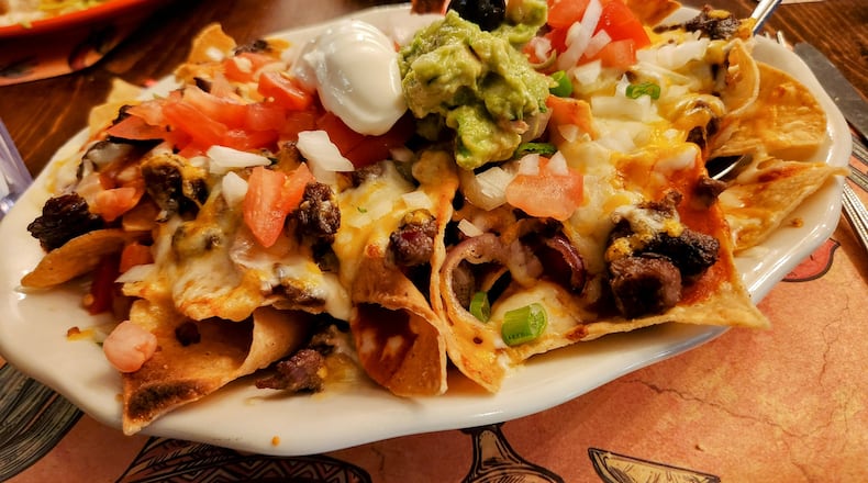 A heaping plate of corn tortilla chips piled high with melted cheese and assorted toppings. ISTOCK