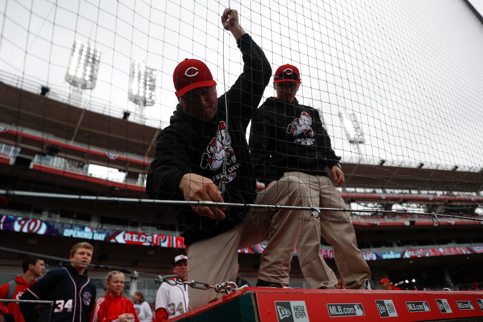 FILE - Members of the grounds crew adjust the new extended netting above the visitors dugout before an opening day baseball game between the Cincinnati Reds and the Washington Nationals, Friday, March 30, 2018, in Cincinnati. (AP Photo/John Minchillo, File)