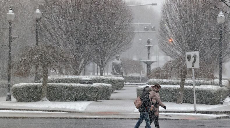 The snow Friday, Feb. 16, 2024 partially obscures two people as they cross Fountain Avenue in downtown Springfield. BILL LACKEY/STAFF