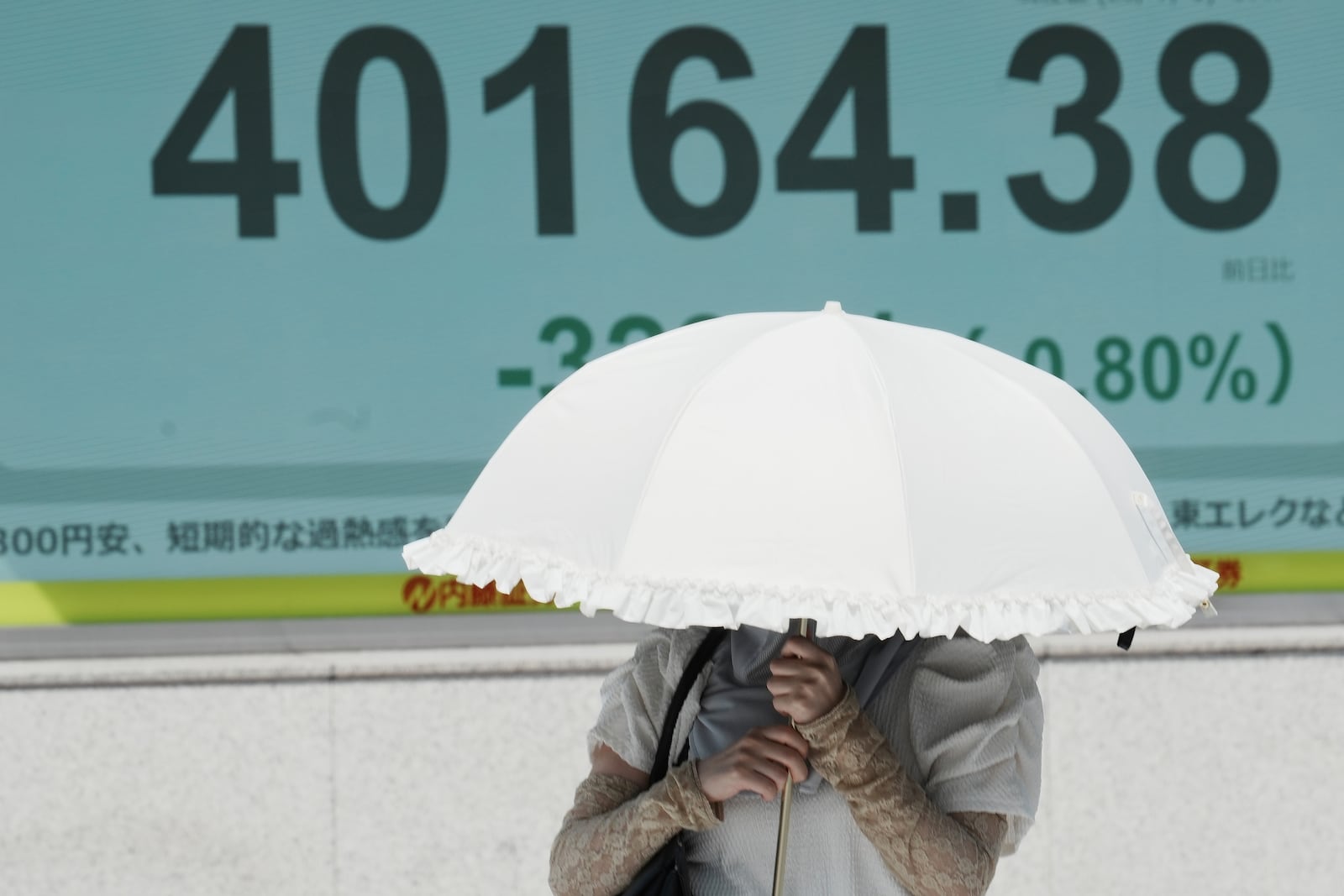 A person walks under the intense sun near an electronic stock board displaying Japan's Nikkei index at a securities firm Tuesday, July 1, 2025, in Tokyo. (AP Photo/Eugene Hoshiko)