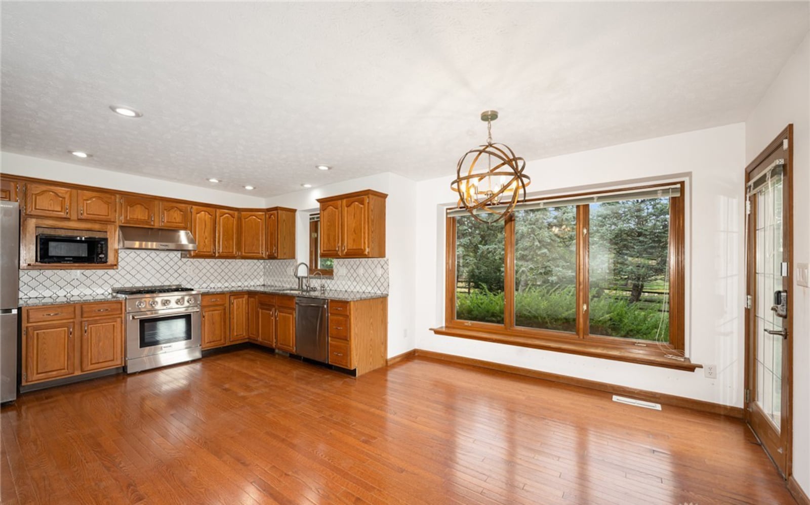 The eat in kitchen has hardwood floors, wood cabinets with granite tops and a tile backsplash. There are professional style appliances including a Thor range and range hood. The breakfast area has a decorative chandelier and exterior door opening to the patio. CONTRIBUTED