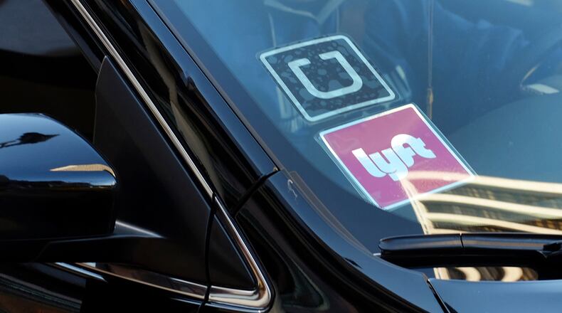 FILE - In this Tuesday, Jan. 12, 2016, file photo, a driver displaying Lyft and Uber stickers on his front windshield drops off a customer in downtown Los Angeles. California regulators on Thursday, Nov. 9, 2017, adopted new safety rules for ride-hailing companies Uber and Lyft that will not require their drivers be fingerprinted as part of background checks, rejecting a push by the taxi industry. (AP Photo/Richard Vogel, File)