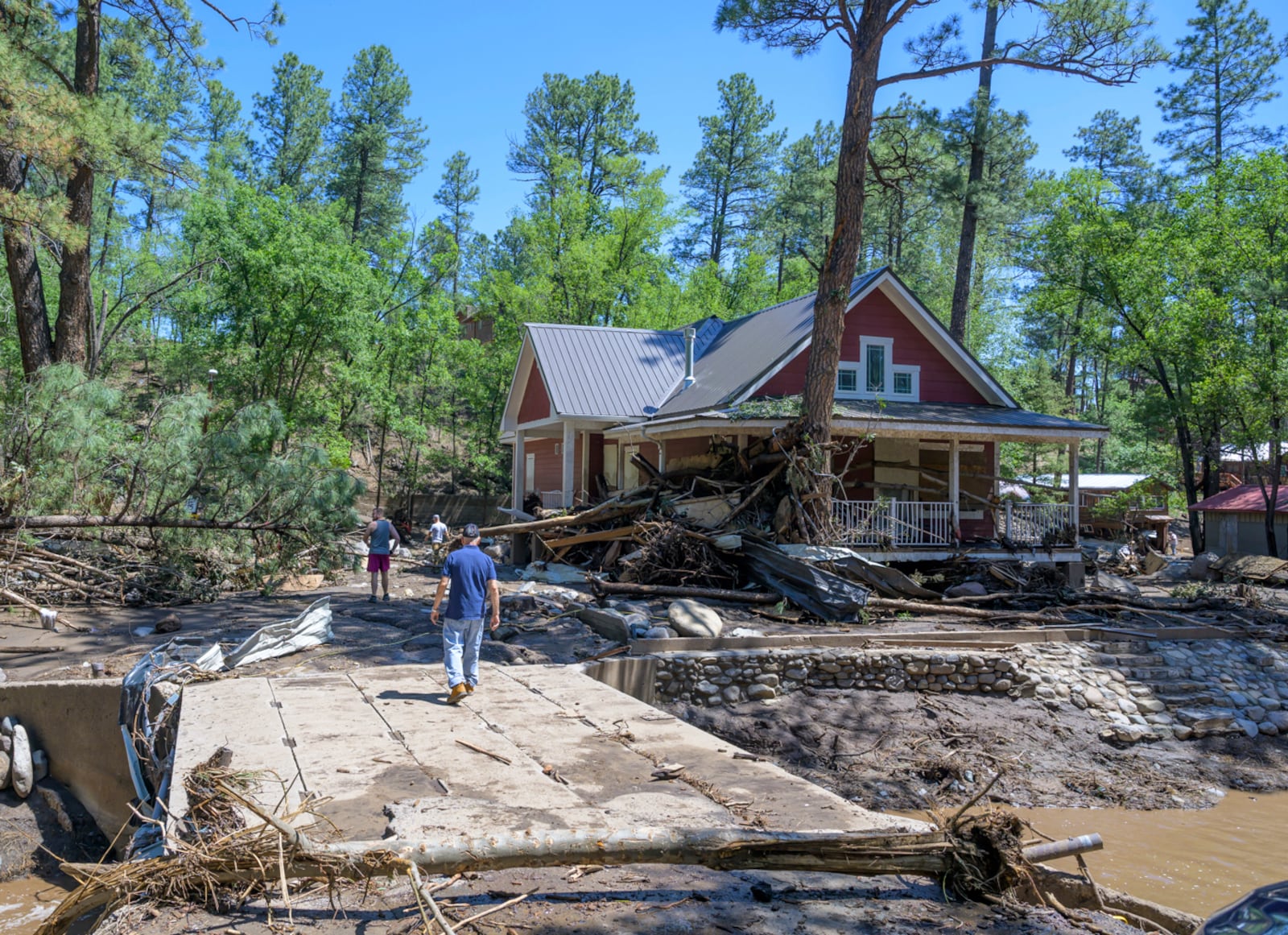 Residents of the town of Ruidoso, N.M., walk back to their neighborhood to find what's left of their homes a day after major flooding washed away properties leaving streets clogged with mud and debris, along the Rio Ruidoso, Wednesday, July 9, 2025, in Ruidoso, N.M. (AP Photo/Roberto E. Rosales)