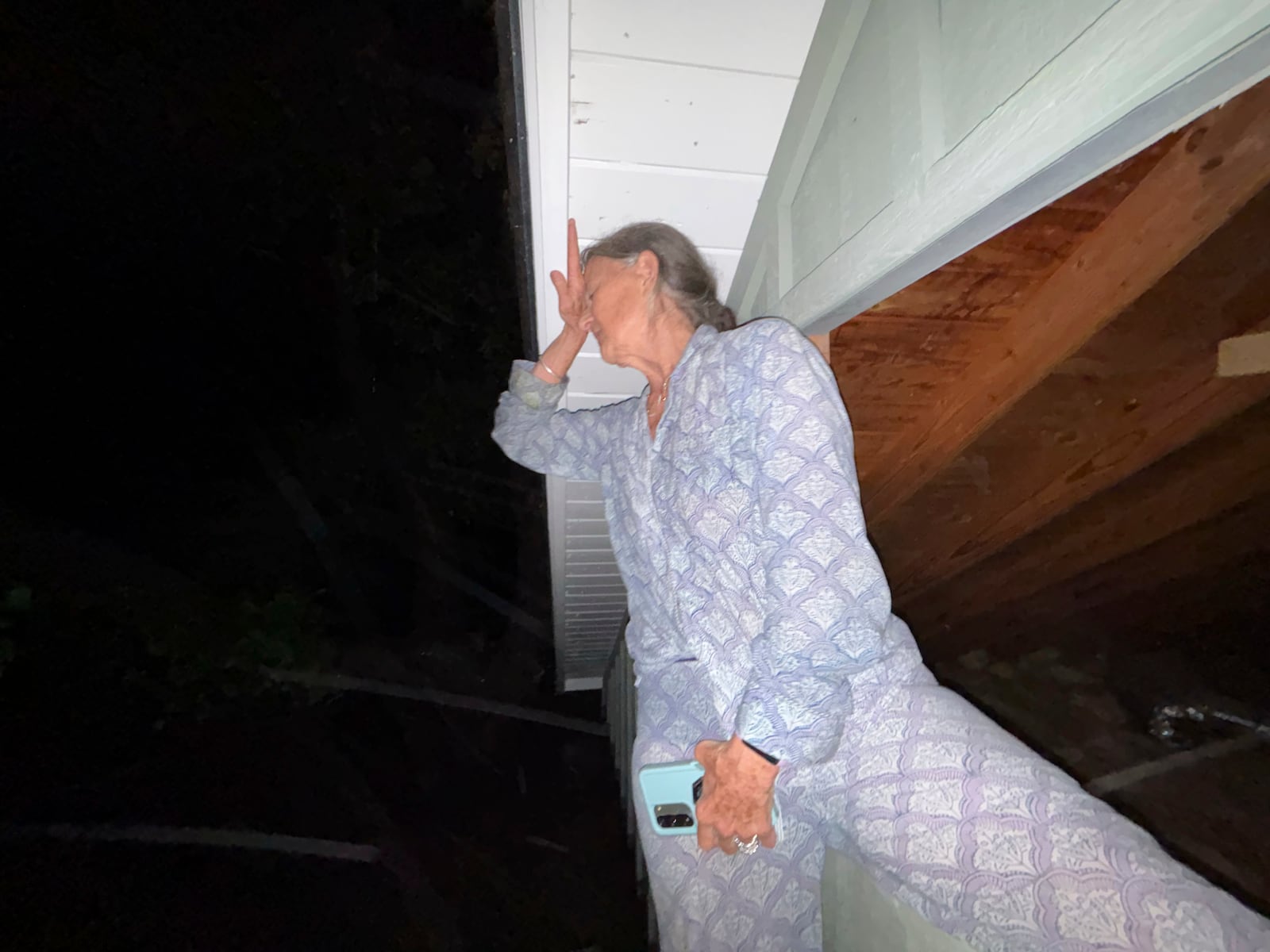 Jane Towler rests her head on an overhang of the roof of her son's cabin, as they escape floodwaters from the Guadalupe River in Hunt, Texas, at 4:56 a.m. on Friday, July 4, 2025. (Shabd Simon-Alexander via AP)