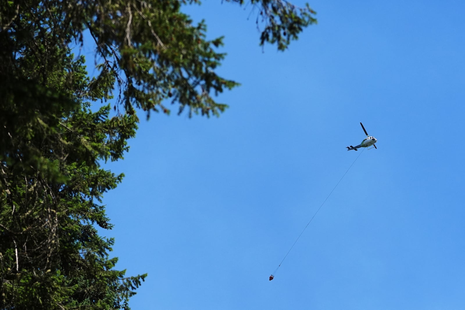 A firefighting helicopter flies over the scene of a wildfire the day after a shooter ambushed and killed multiple firefighters responding to the wildfire at Canfield Mountain Monday, June 30, 2025, in Coeur D'Alene, Idaho. (AP Photo/Lindsey Wasson)