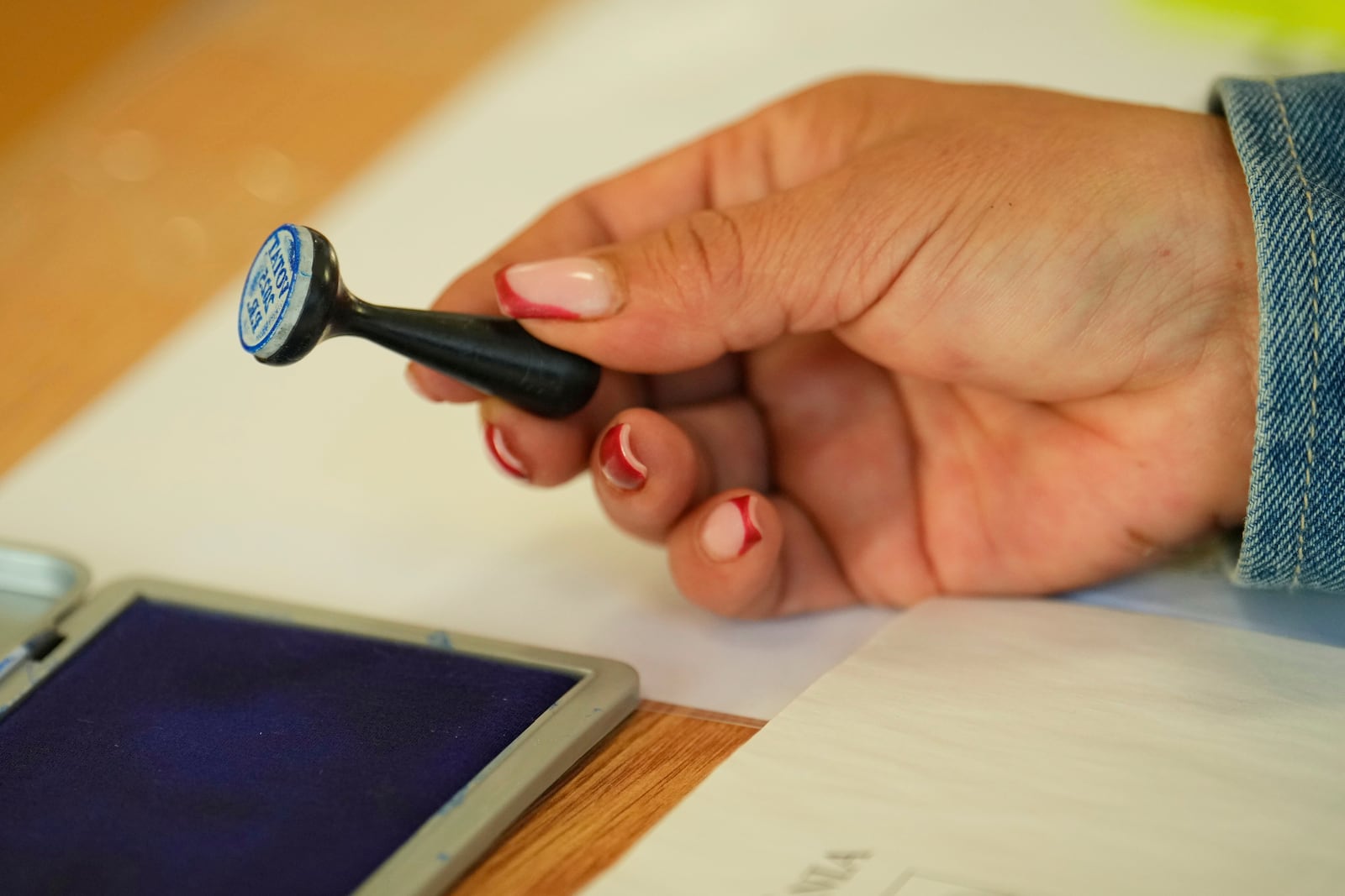 An election official holds a voting stamp while waiting for people to vote in the first round of the presidential election redo in Mogosoaia, Romania, Sunday, May 4, 2025. (AP Photo/Vadim Ghirda)