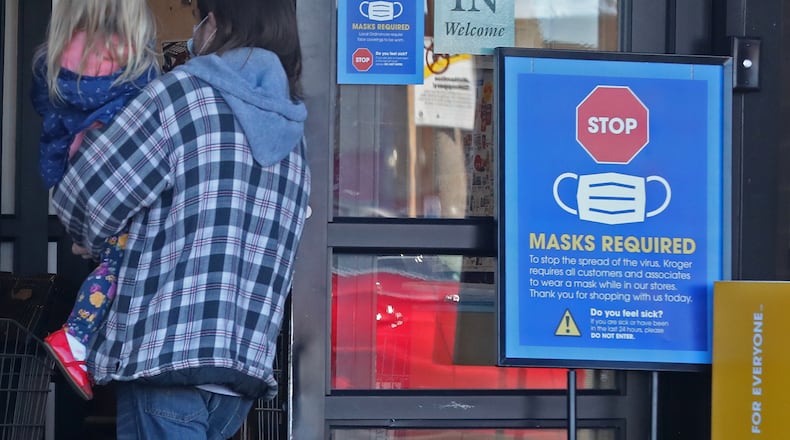 A man carries his daughter into a business that requires masks. BILL LACKEY/STAFF