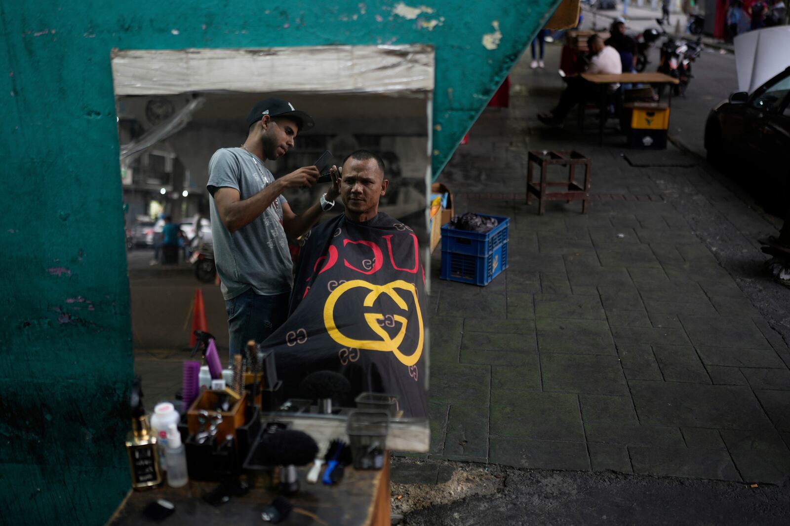 John Rodriguez cuts a client's hair under the Fuerzas Armadas bridge in Caracas, Venezuela, Thursday, April 10, 2025. (AP Photo/Ariana Cubillos)