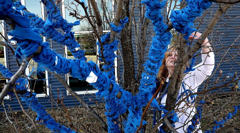Kristi Limes wraps branches of a tree in front of the Hollenbeck-Bayley Conference Center with blue ribbons as she works on the Project Jericho Blue Ribbon Tree for Child Abuse Awareness Month. BILL LACKEY/STAFF