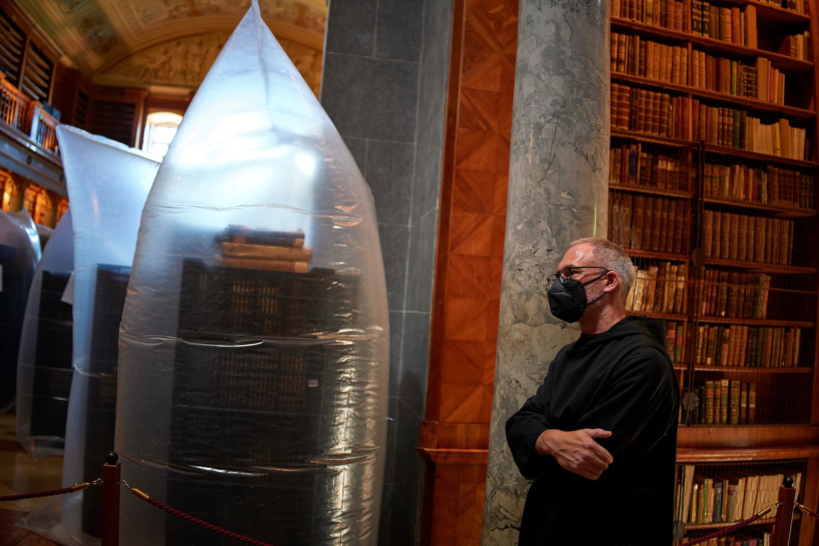 A priest wearing a face mask stands by books kept in hermetically sealed plastic sacks for disinfection at the Pannonhalma Archabbey's library in Pannonhalma, Hungary, Thursday, July 3, 2025, as a beetle infestation threatens its ancient collection. (AP Photo/Bela Szandelszky)