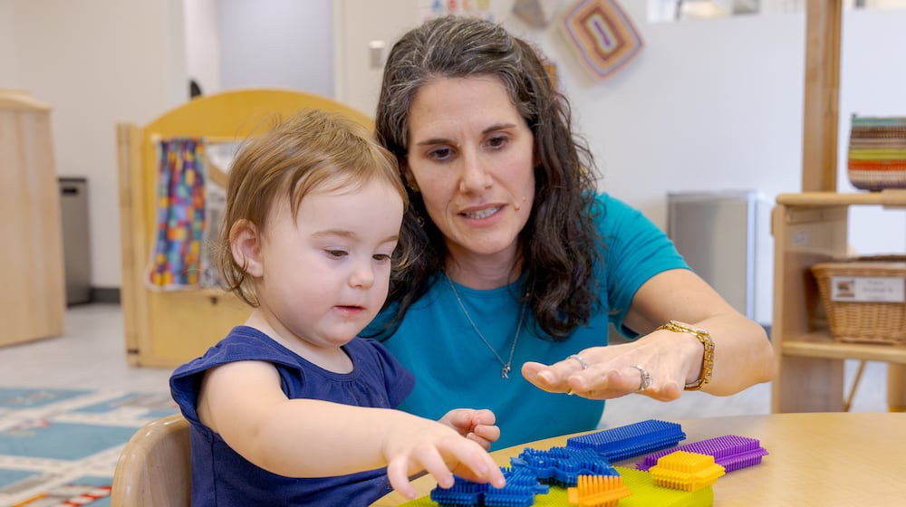 Nicole Myrick, director of Mini University at Sinclair Community College, explains a toy to a child on Tuesday, March 10. Childcare providers in Ohio have always had small profit margins, but new regulations have increased both the amount of hours required to hit reimbursement and the amount of money reimbursed, challenging some childcare providers. BRYANT BILLING / STAFF