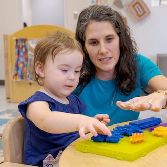 Nicole Myrick, director of Mini University at Sinclair Community College, explains a toy to a child on Tuesday, March 10. Childcare providers in Ohio have always had small profit margins, but new regulations have increased both the amount of hours required to hit reimbursement and the amount of money reimbursed, challenging some childcare providers. BRYANT BILLING / STAFF
