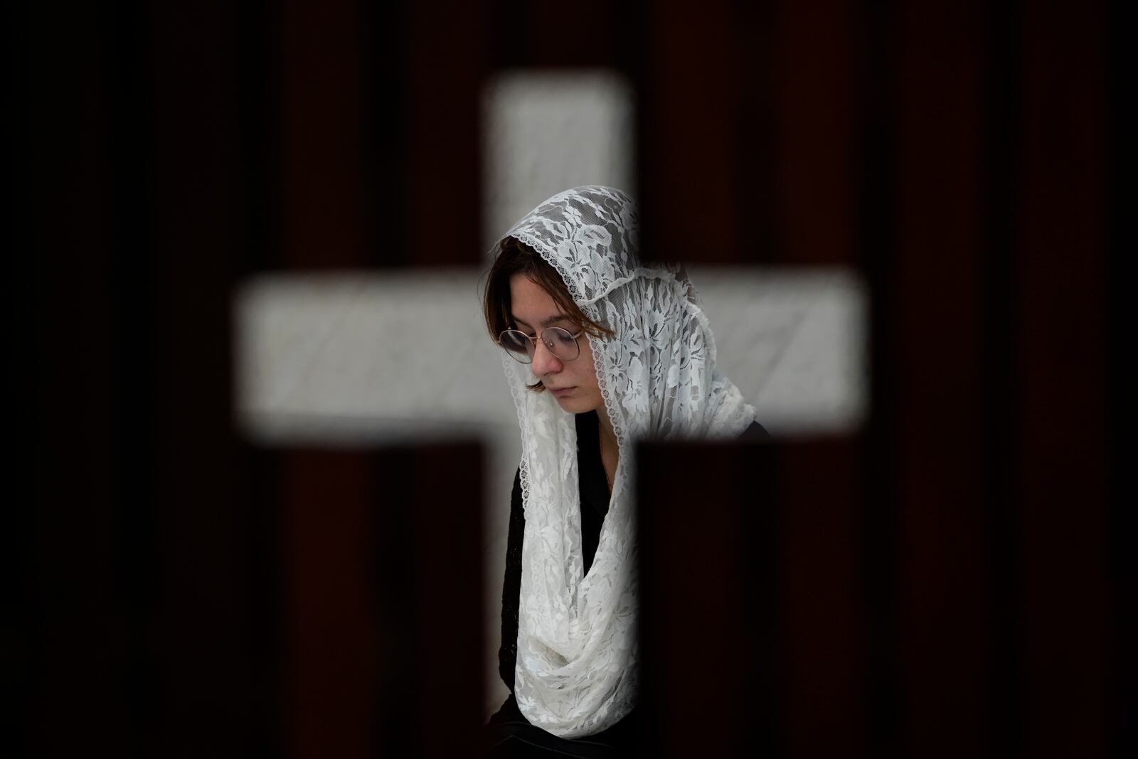 Photographed through an opening in the shape of a cross, a person prays during Mass in honor of Pope Francis, following the Vatican's announcement of his death, at the Cathedral in Brasilia, Brazil, Monday, April 21, 2025. (AP Photo/Eraldo Peres)