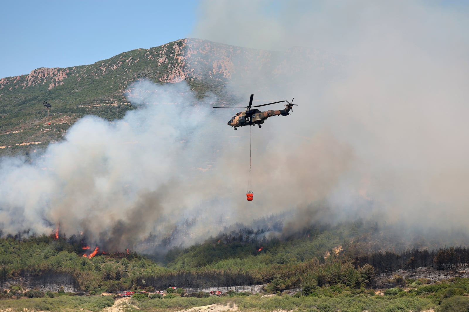 A helicopter sprays water to extinguish a fire in Seferihisar, near Izmir, Turkey, Monday, June 30, 2025. (Cengiz Malgir/Dia Photo via AP)