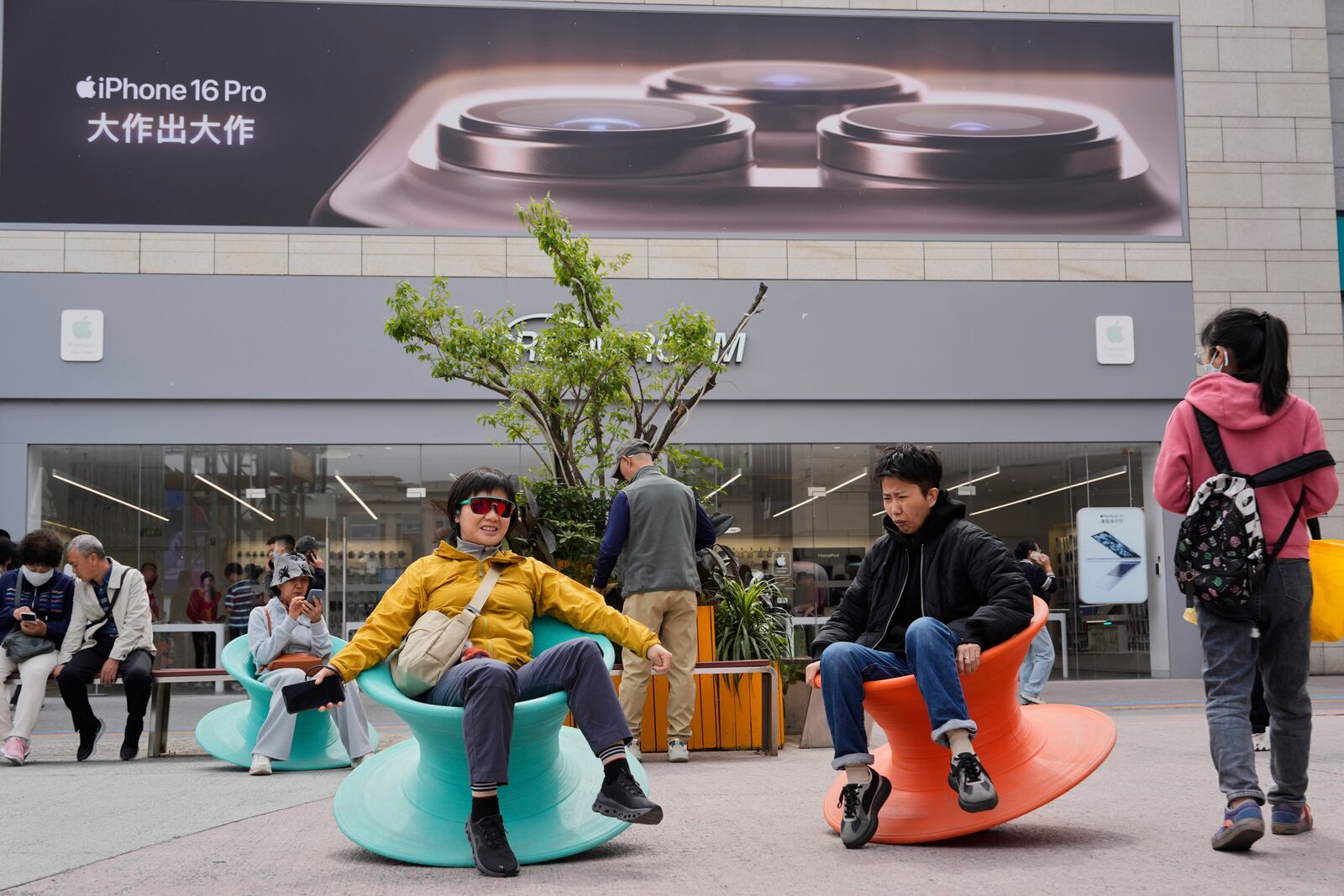 Shoppers balance themselves on wobbling seats near a store selling Apple products in Beijing, China, Tuesday, April 8, 2025. (AP Photo/Ng Han Guan)