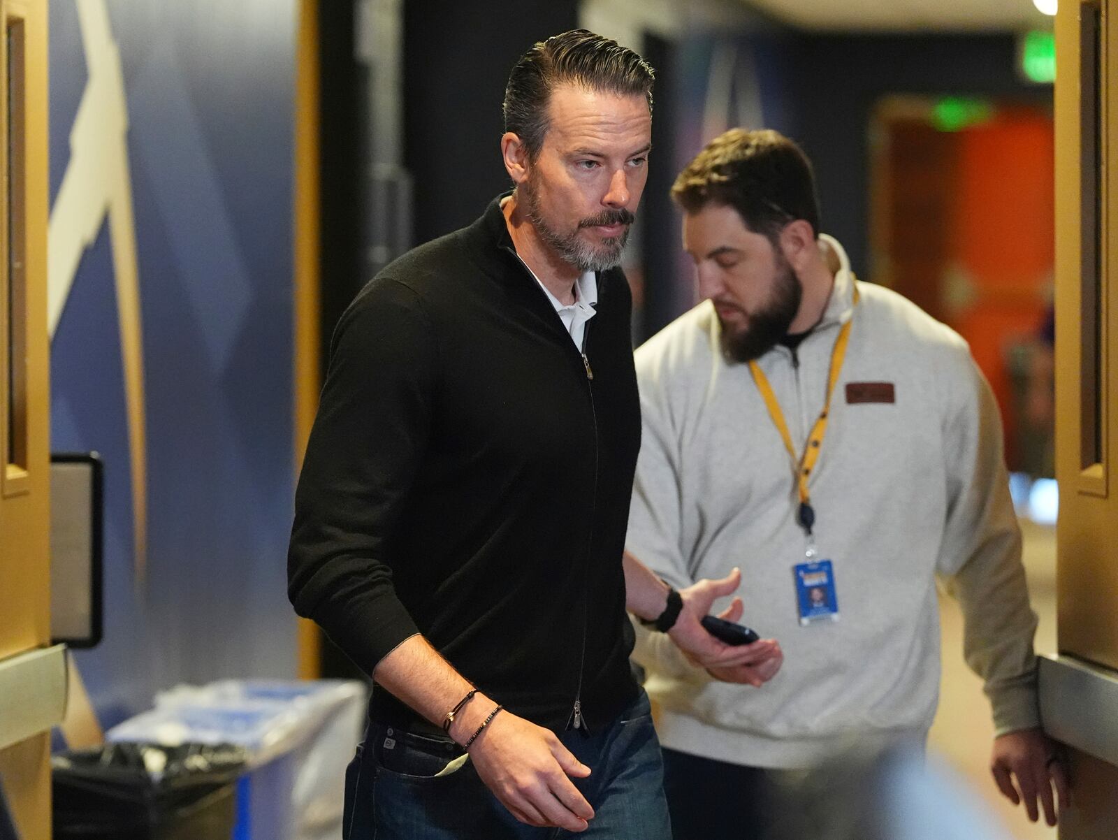 Denver Nuggets team president Josh Kroenke, left, hands off his mobile phone to the Nuggets' media relations manager Nick O'Hayre on the way in to respond at a news conference Monday, April 14, 2025, in Denver to questions about the firing of the team's general manager and head coach last week. (AP Photo/David Zalubowski)
