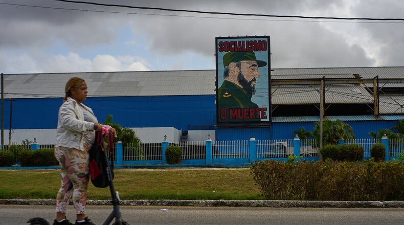 A woman rides an electric scooter past a factory displaying an image depicting the late Cuban leader Fidel Castro, bearing the words "Socialism or Death", in Havana, Cuba, Thursday, March 19, 2026. (AP Photo/Ramon Espinosa)