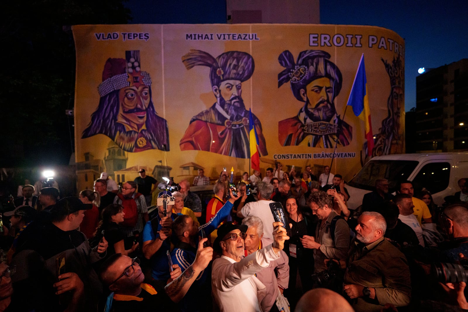 Supporters of presidential candidate George Simion react to the exit poll results, backdropped by depictions of Romanian historical figures, outside the headquarters of the Alliance for the Unity of Romanians (AUR) after polls closed for the first round of the country's presidential election redo in Bucharest, Romania, Sunday, May 4, 2025. (AP Photo/Andreea Alexandru)